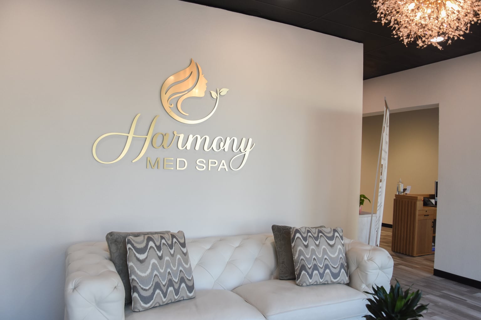 Harmony Med Spa gold wall logo above a sofa and patterned cushions in the waiting area