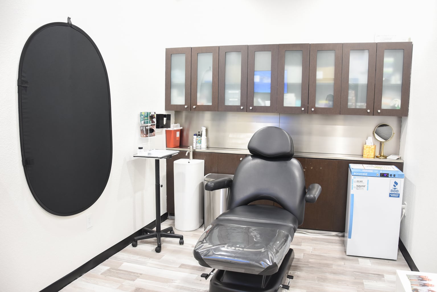 Gray reclining treatment chair with dark glass-front cabinets at Harmony Med Spa